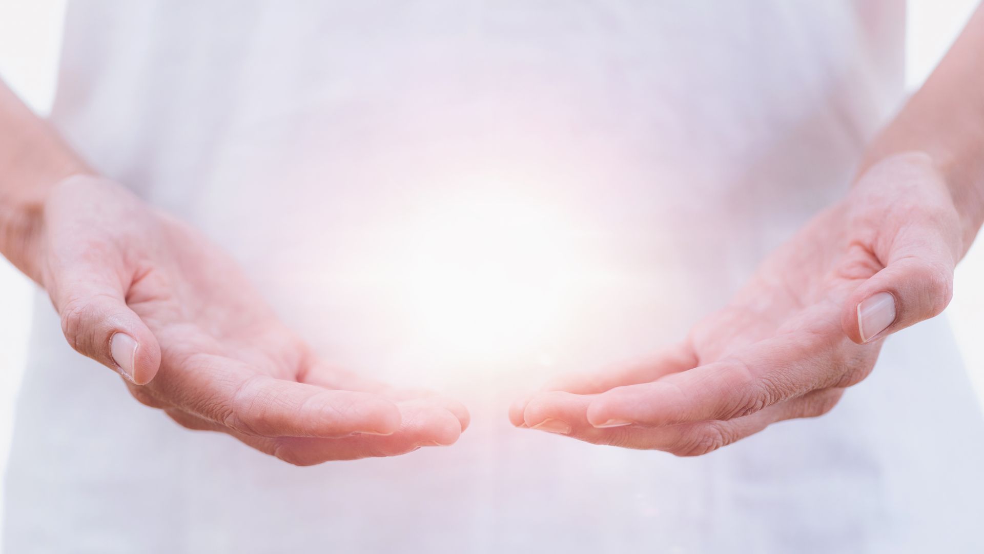 A ball of light glows between the hands of a woman in a white gown