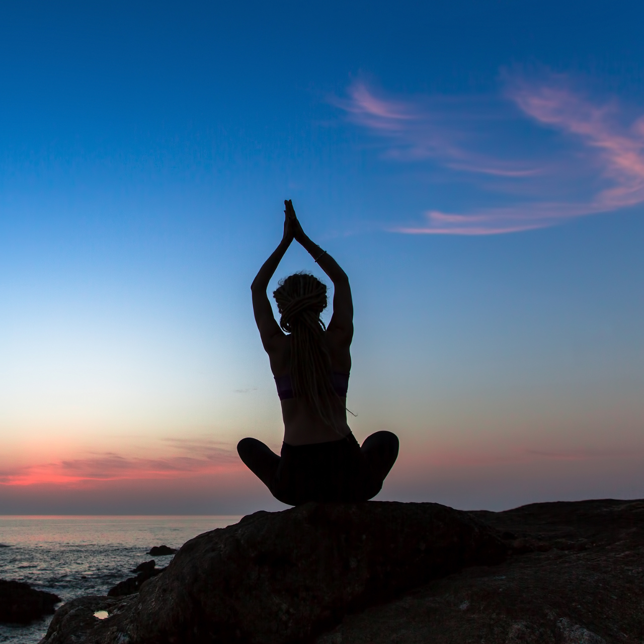 Silhouette of a young woman practicing yoga exercises on the ocean at twilight.