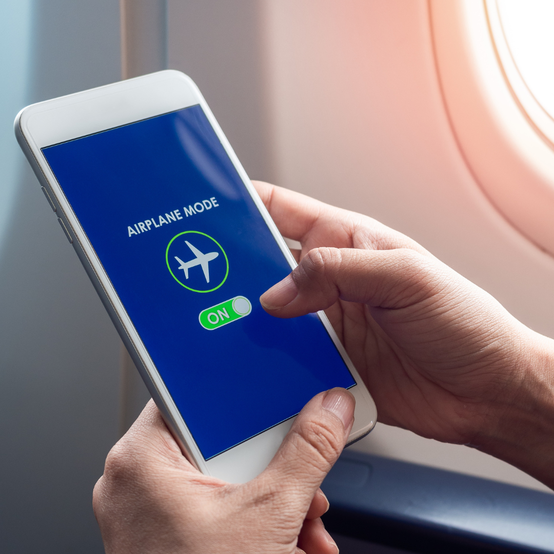 Flight mode concept. Hand holding white smartphone and turned on airplane mode on screen near the window on the airplane