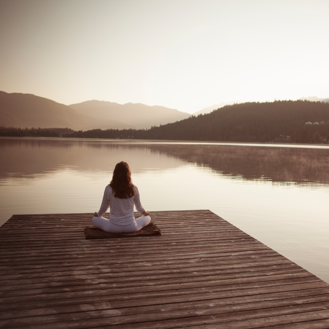 Woman meditating by lake.