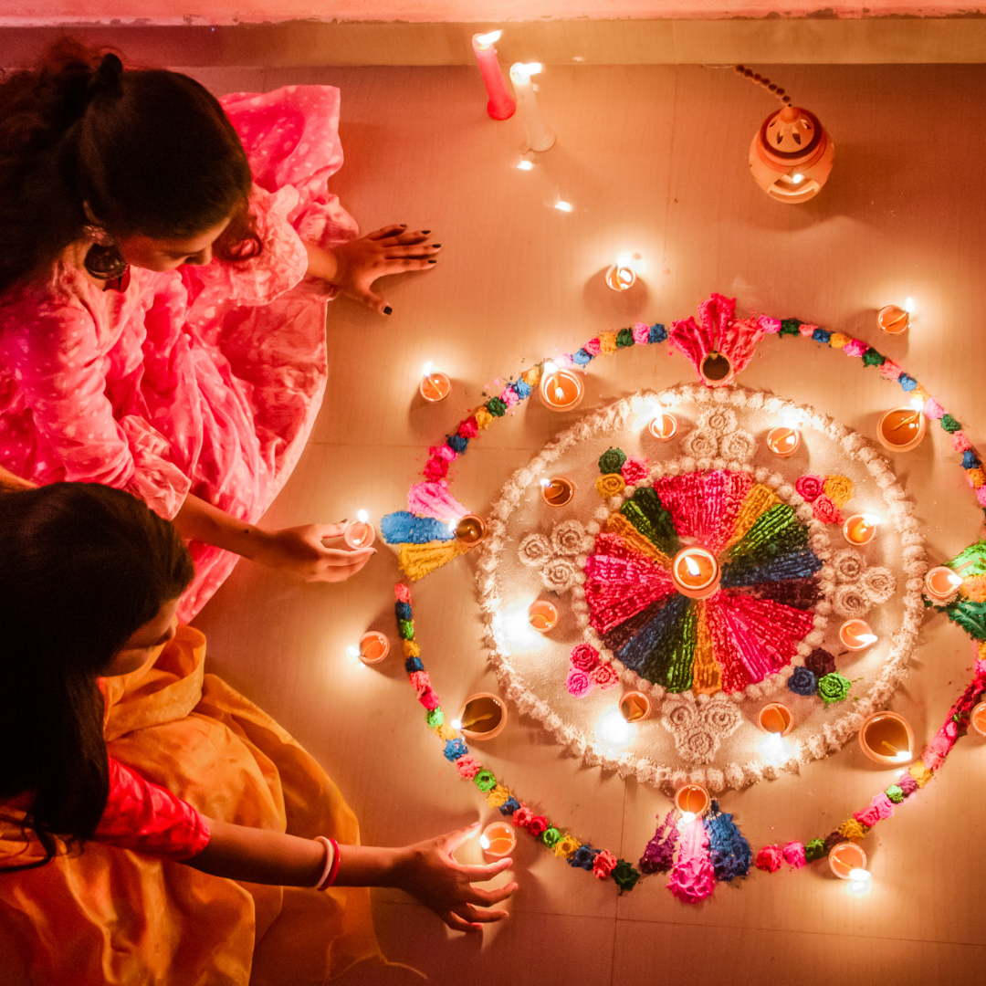 Women Sitting on the Floor Holding Candles Beside Colorful Flowers During Diwali Festival