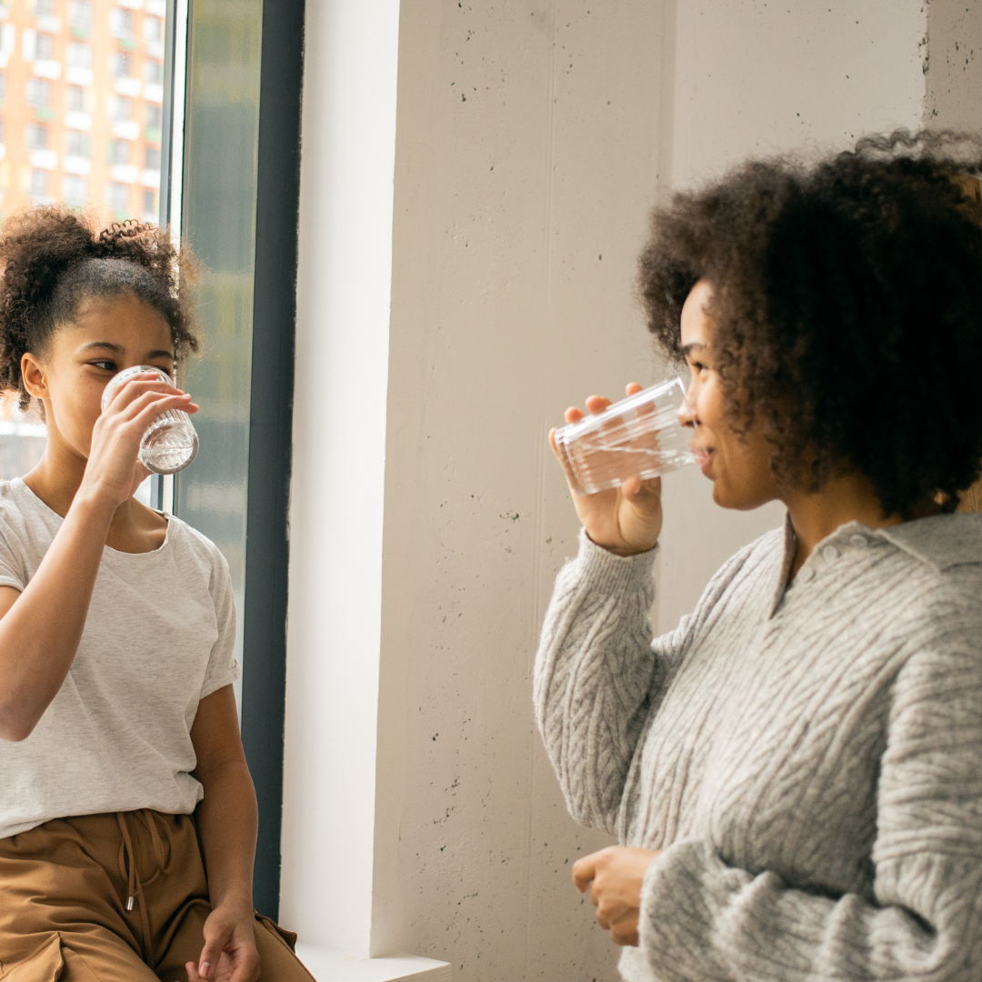 Content black woman with daughter drinking water near window