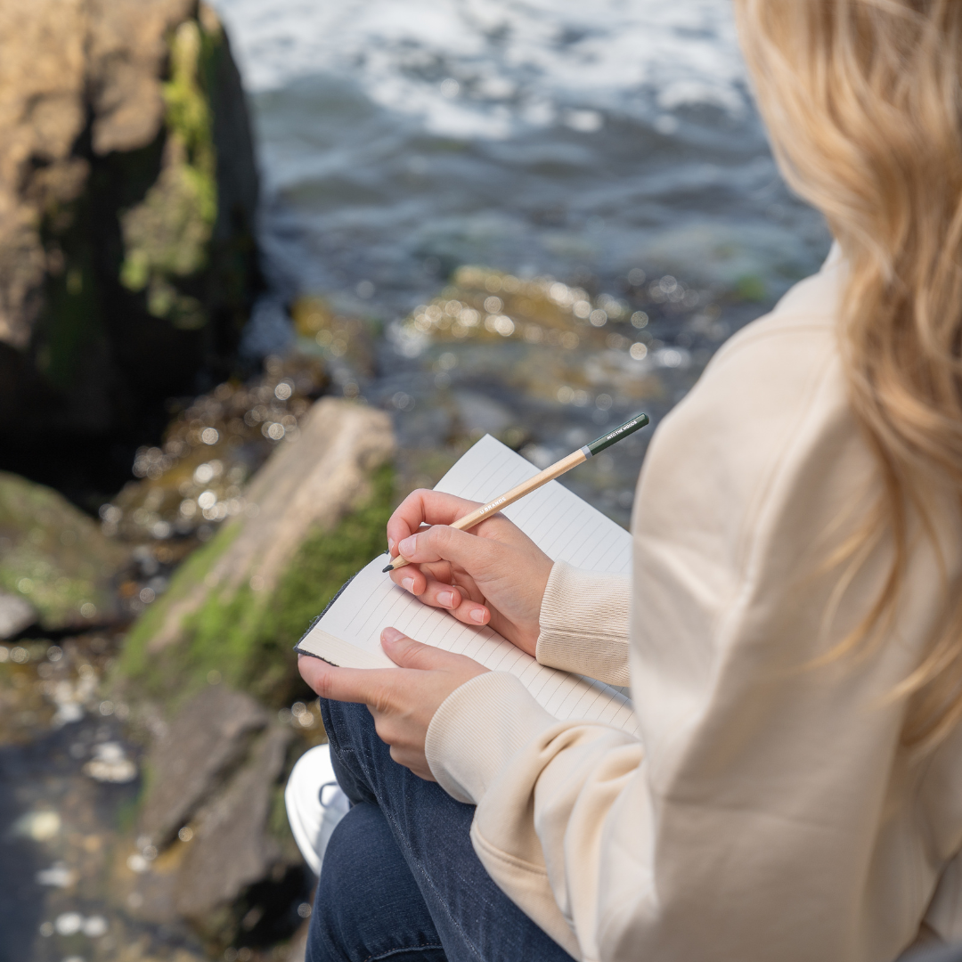 Woman Sitting By the Water and Writing in a Journal