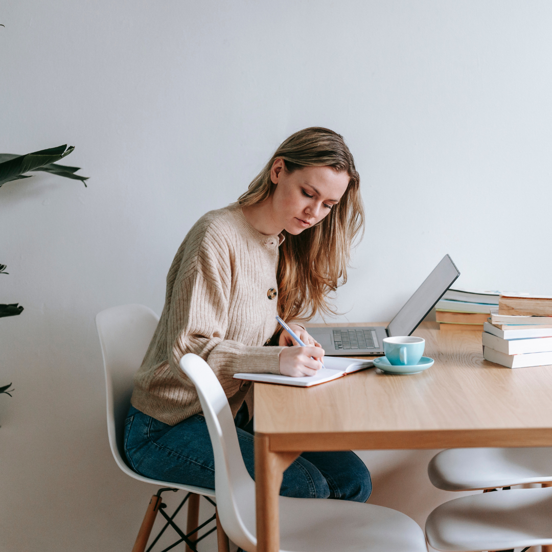 Focused woman writing in notebook at table with laptop