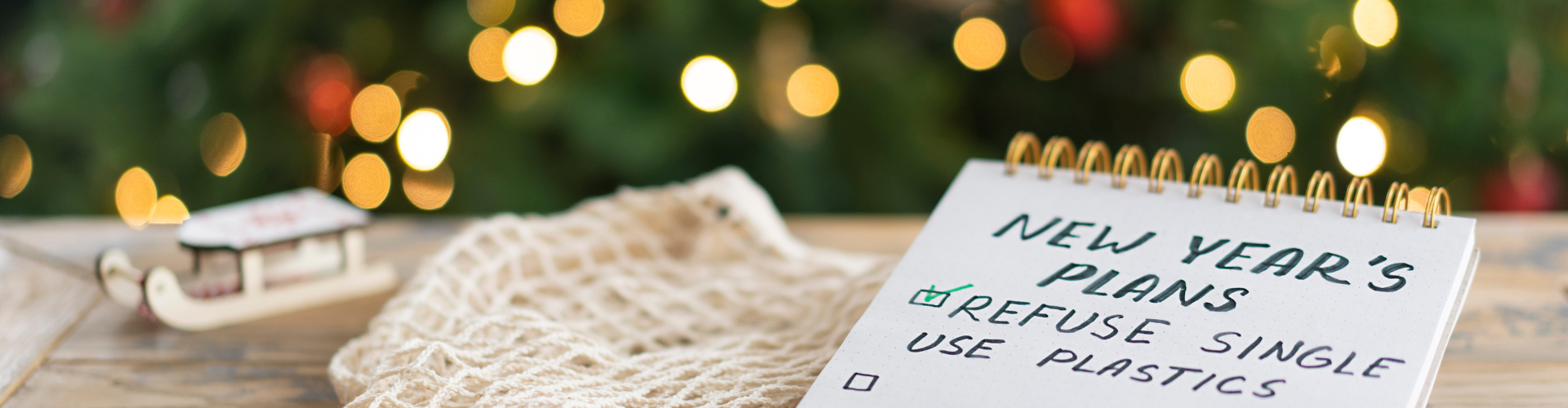 Notepad on the wooden background with plans for the next year and the inscription - new year goals - refuse single use plastics and natural Christmas decoration