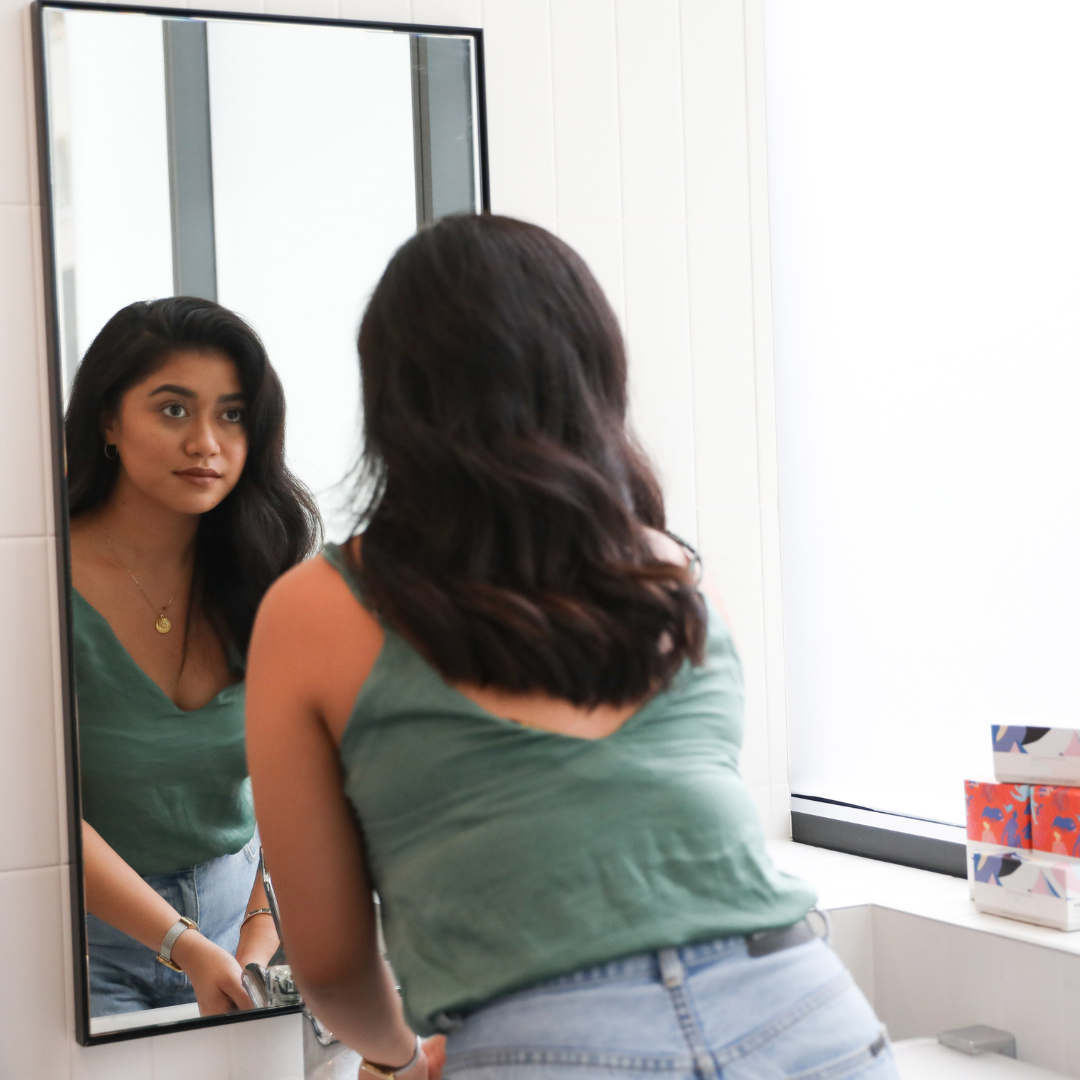 Woman looking at self in mirror in office toilet