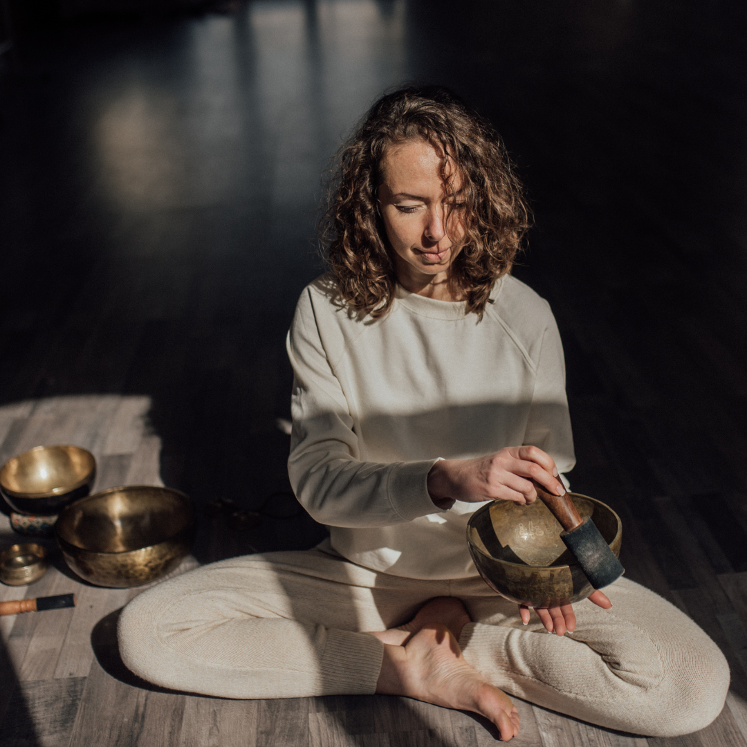 Spiritual practitioner playing bowl gong on floor in sunlight