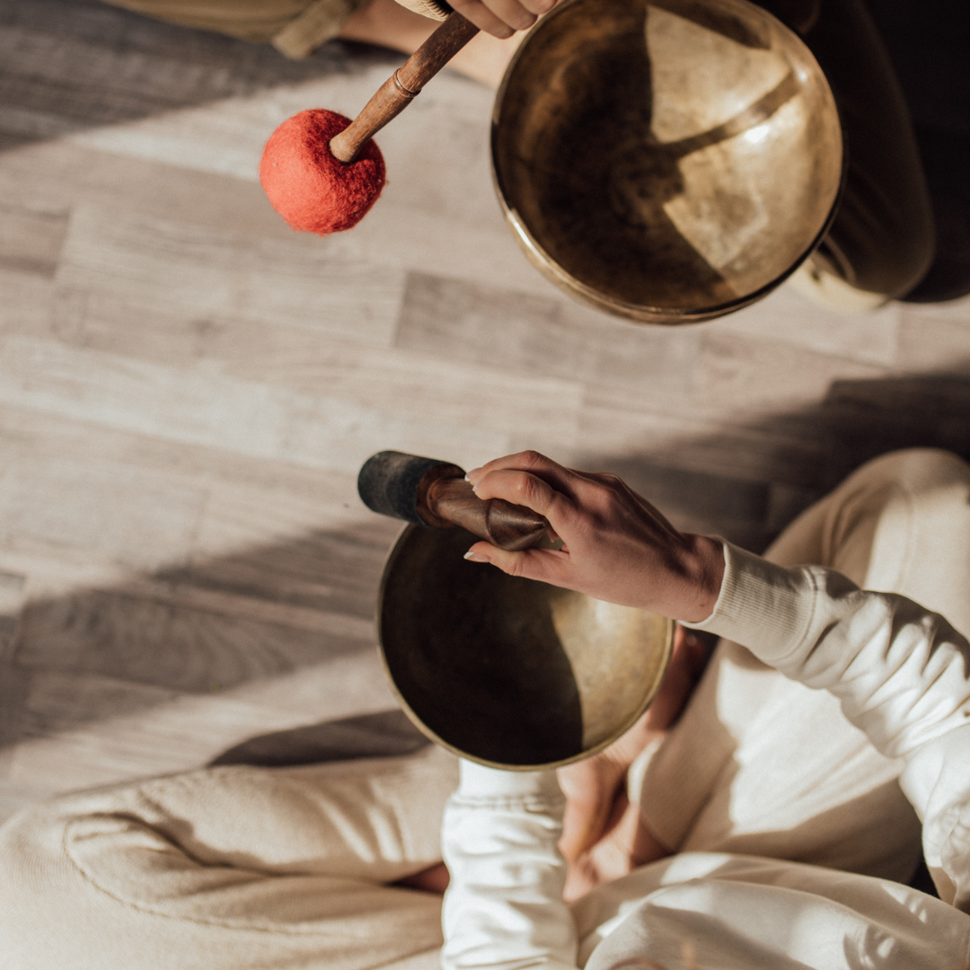 Two People Sitting on Floor Using Tibetan Singing Bowls