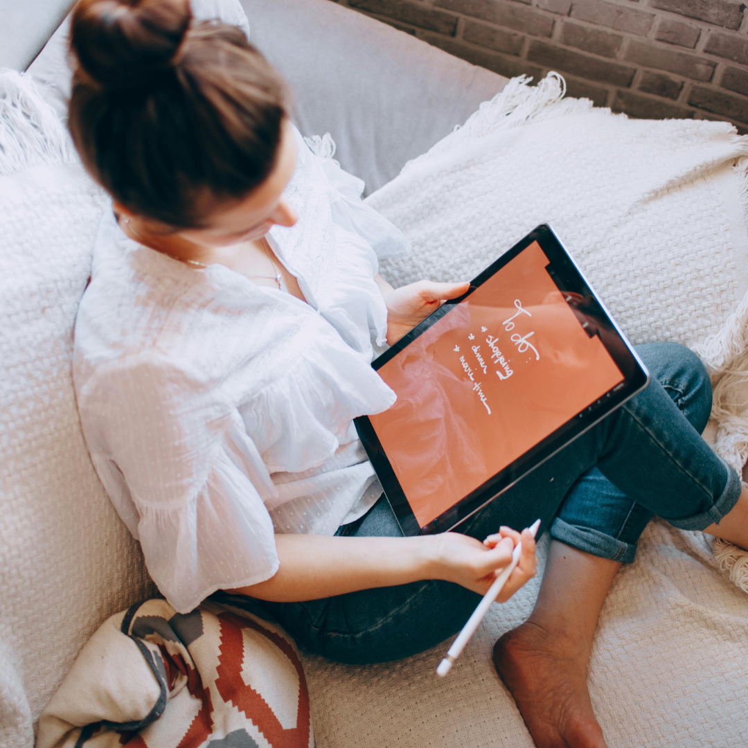 Woman Writing To Do List on Tablet Sitting on Sofa