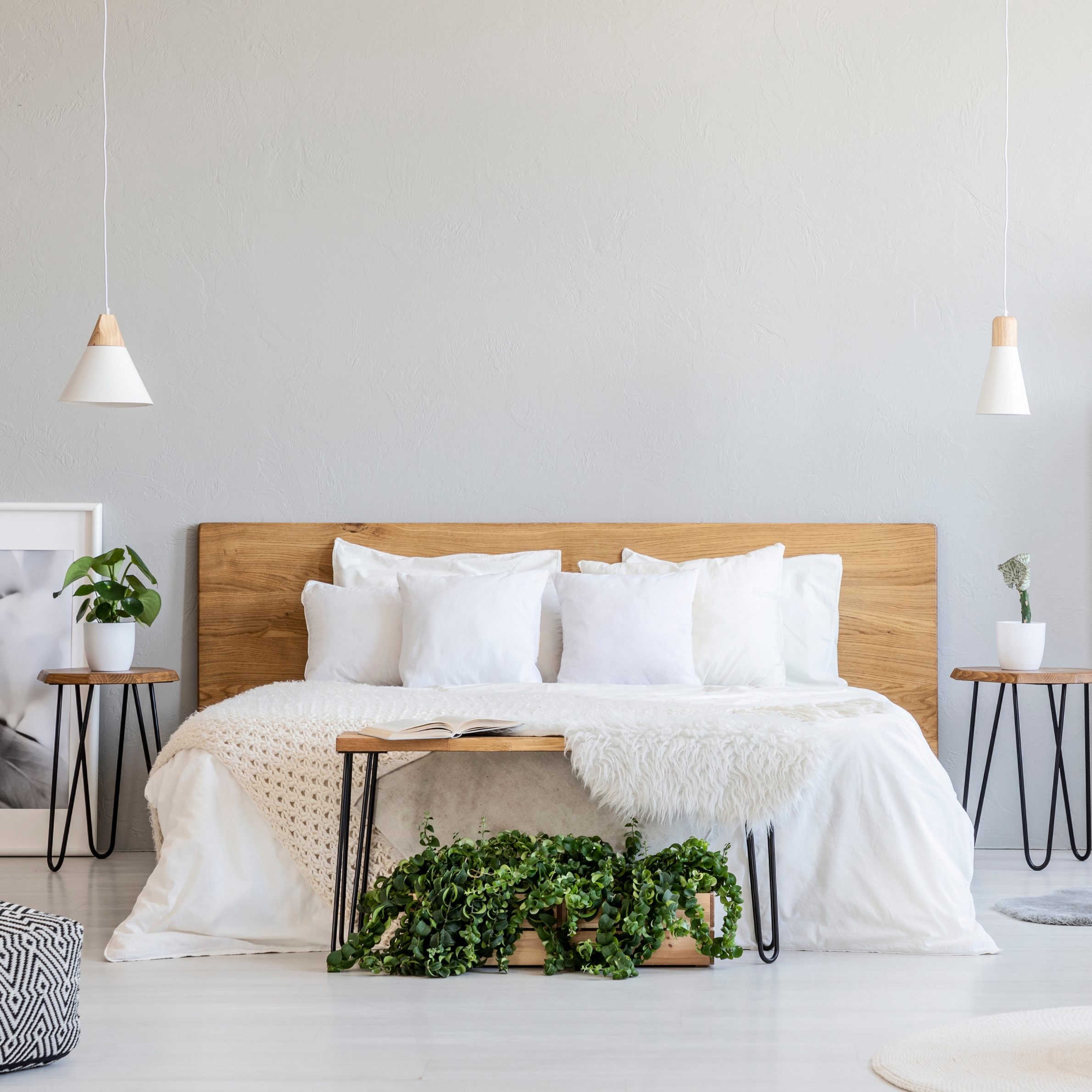Patterned pouf and basket in bright bedroom interior with lamps, plants and poster next to bed. Real photo