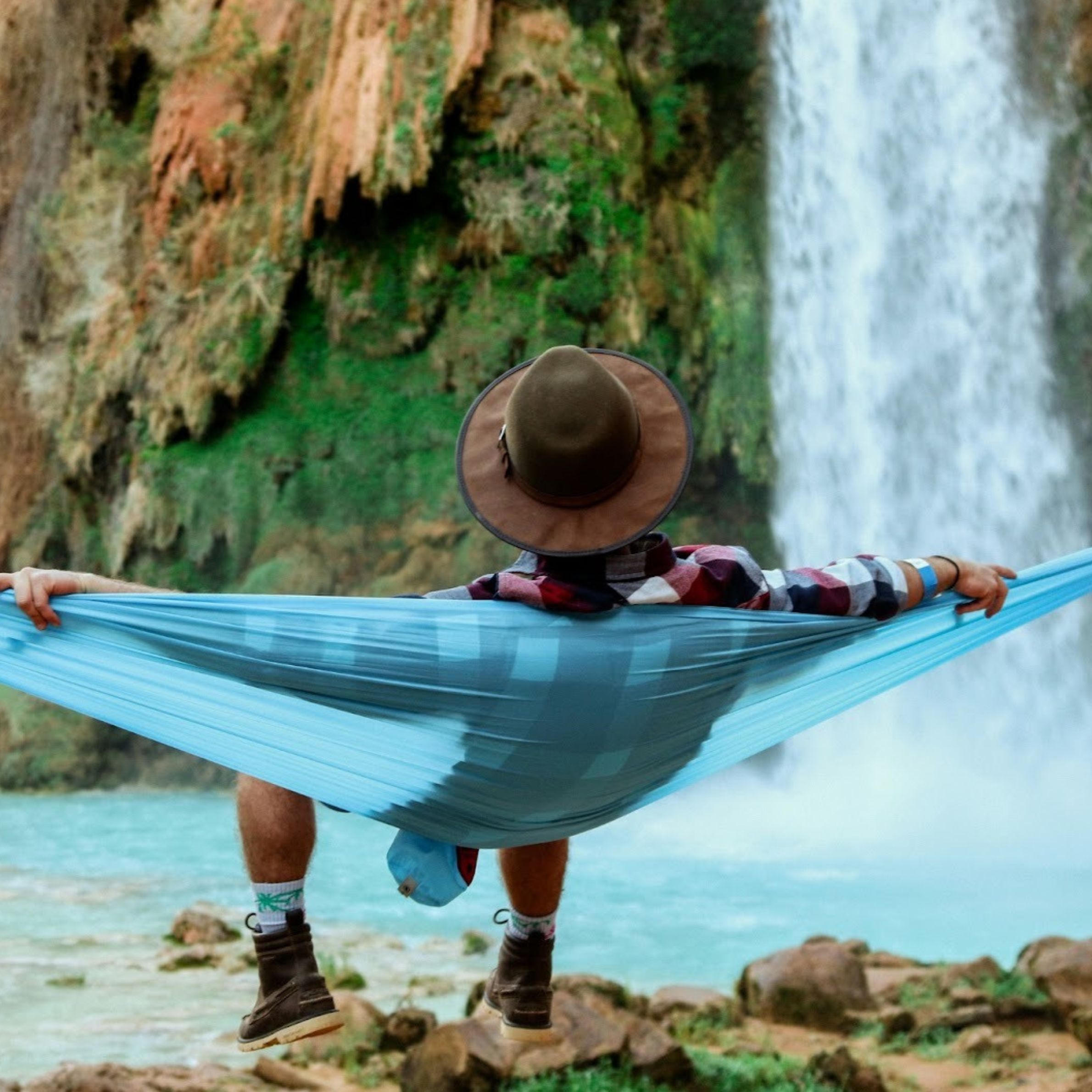 man lying on hammock near waterfalls
