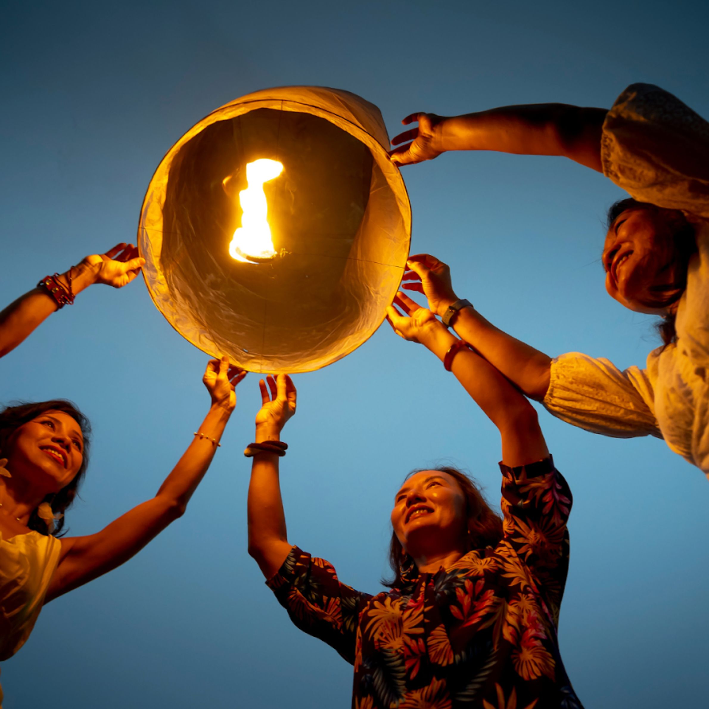 Group of people releasing a sky lantern at dusk, symbolizing collective energy, intention, and connection