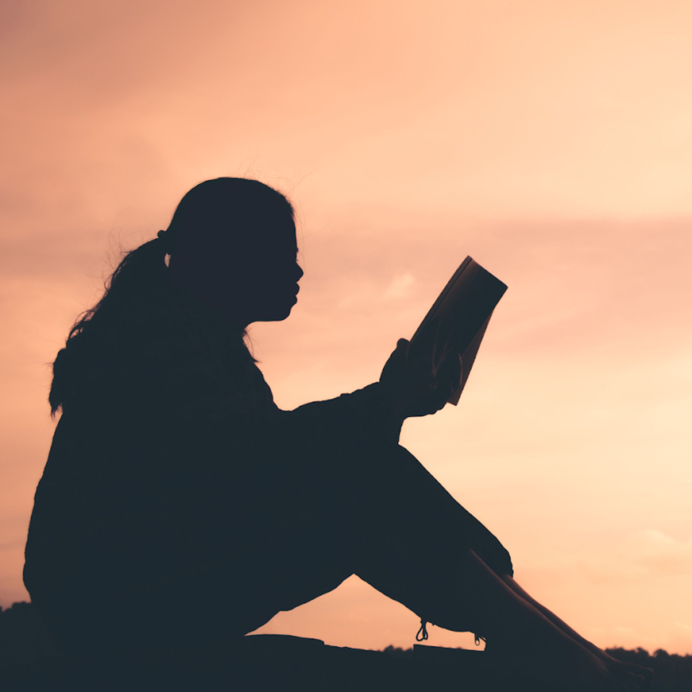 Silhouette of a person reading at sunset, reflecting inner awareness, learning, and personal transformation