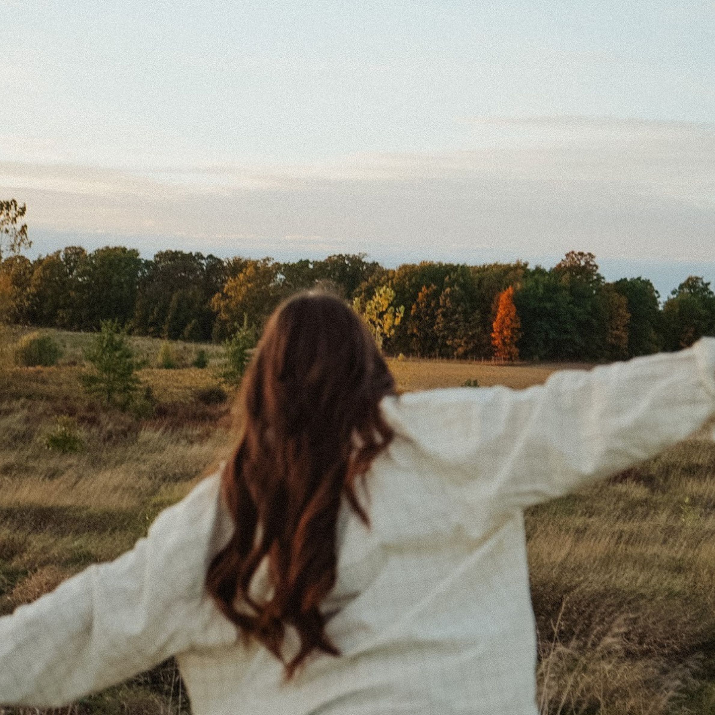 Woman standing in nature with arms outstretched, representing freedom, presence, and connection to energy